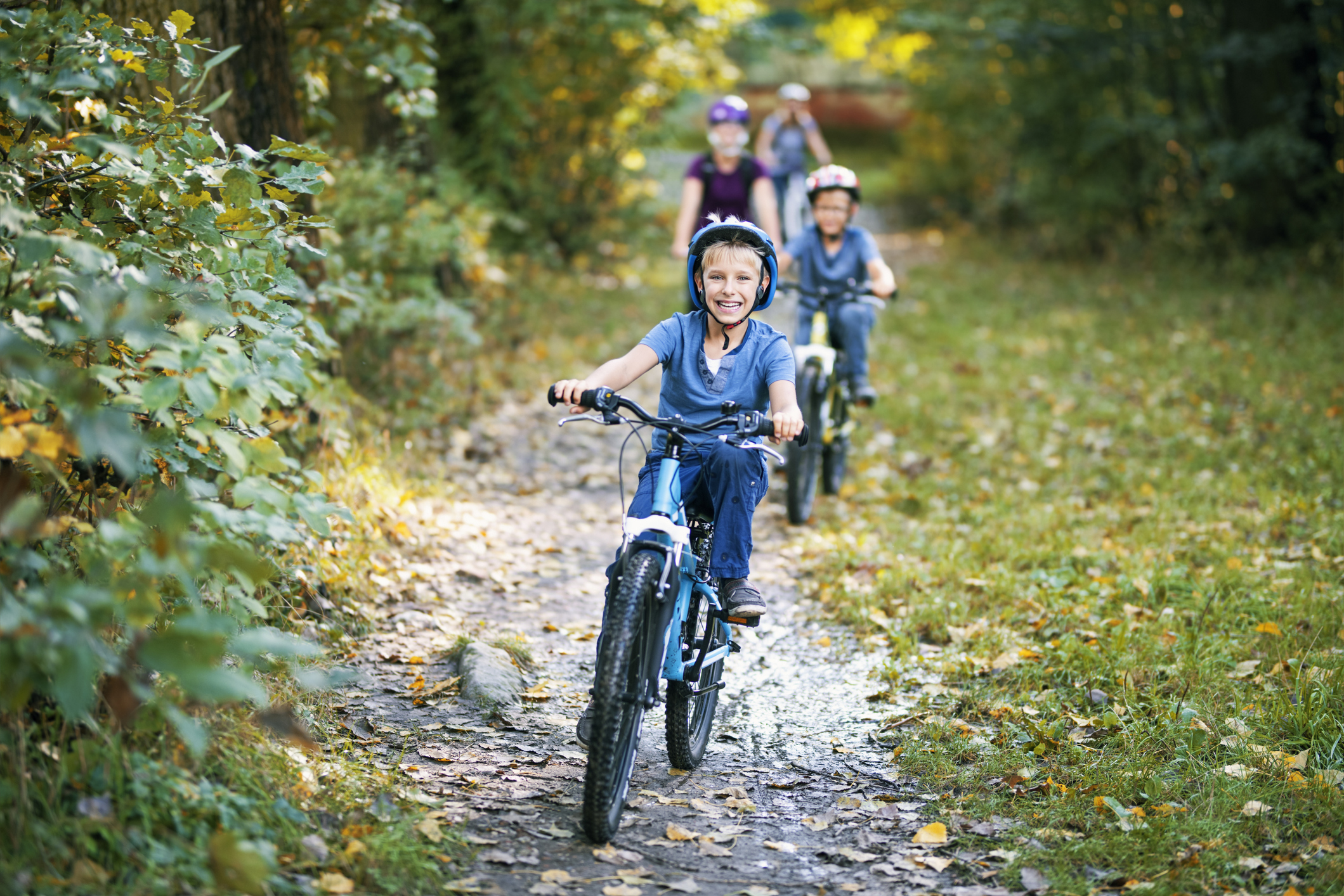 Little boy and his family riding bicycles in nature. The boy is smiling happily.
Nikon D810
