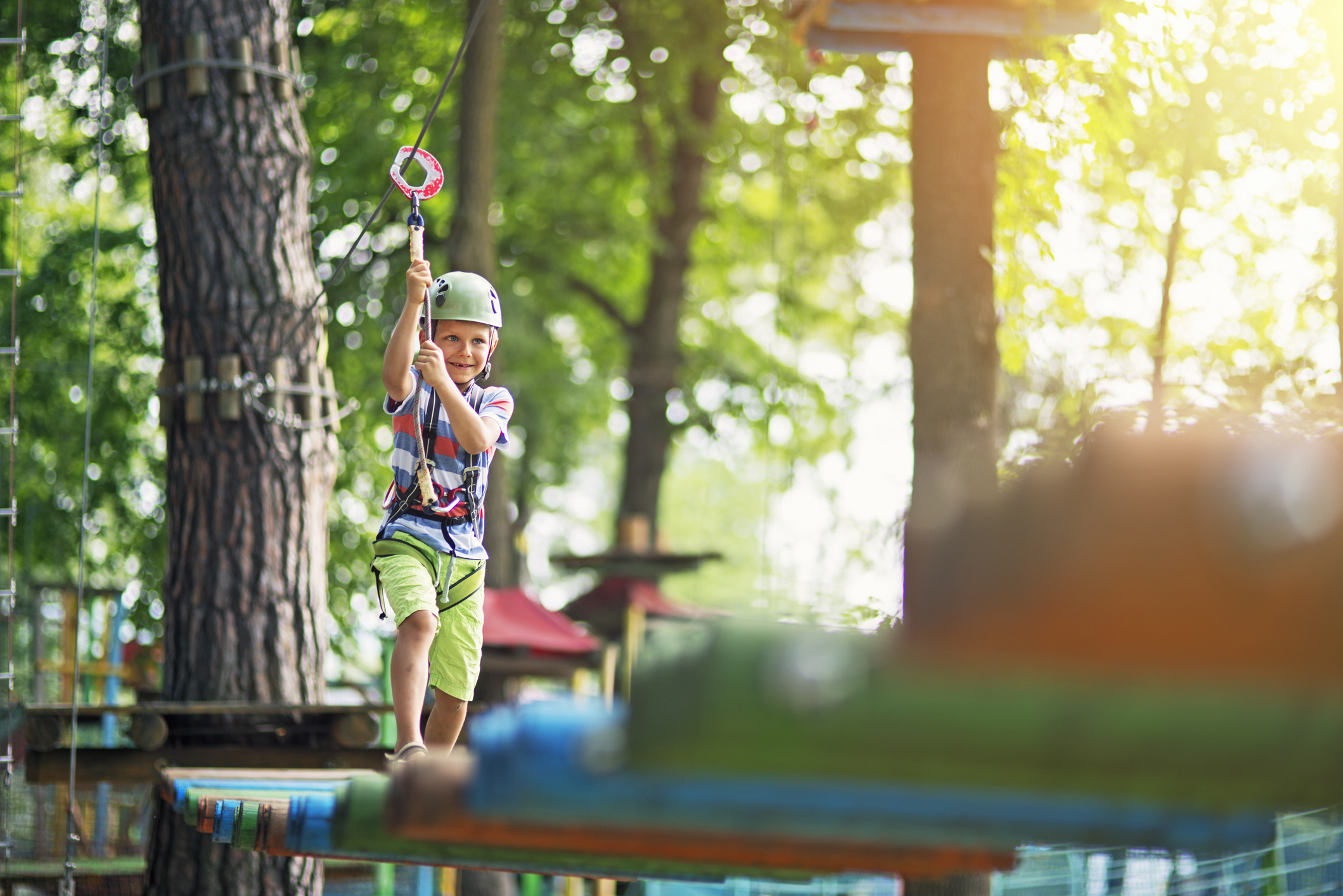 Little boy participating in ropes course in outdoors adventure park. The boy aged 7 is smiling. Sunny summer day.